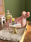 Ballerina mouse relaxing on a cushion next to a tiny table with pink cups and fresh flowers
