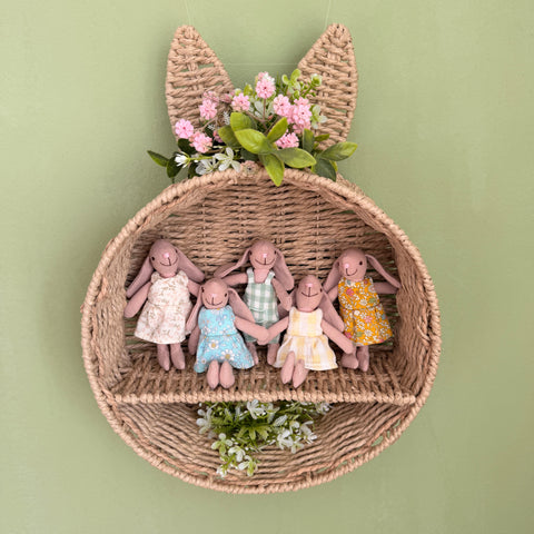 Fünf handgemachte Stoffhasen in Blumenkleidern sitzen in einem geflochtenen Wandkorb in Hasenform